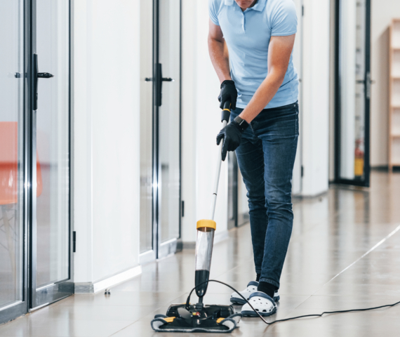 Korteriühistu hoolduskoristus 3 Young man works in the modern office. Uses vacuum cleaner.